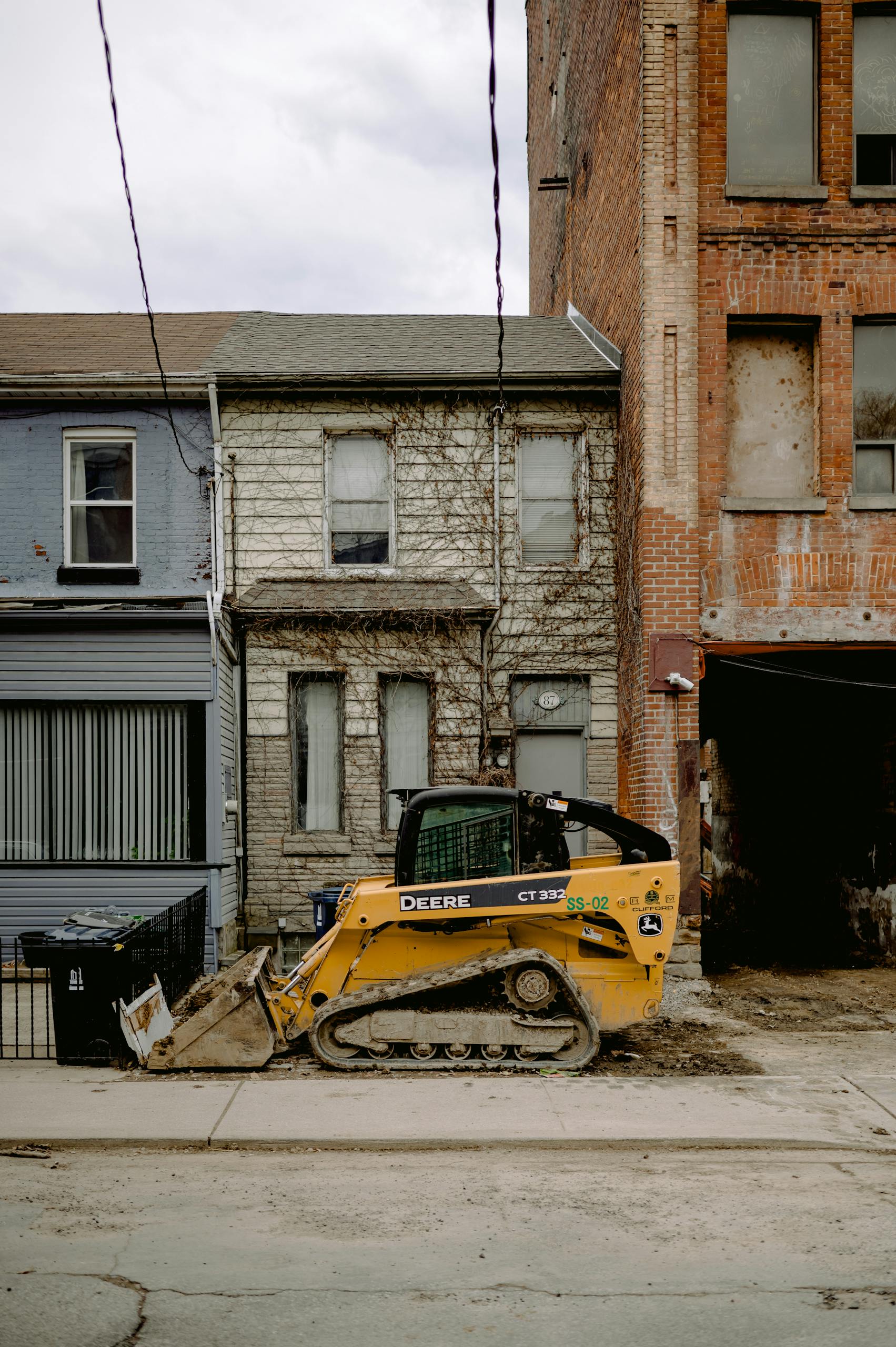 A yellow bulldozer parked on an urban street between old brick buildings.